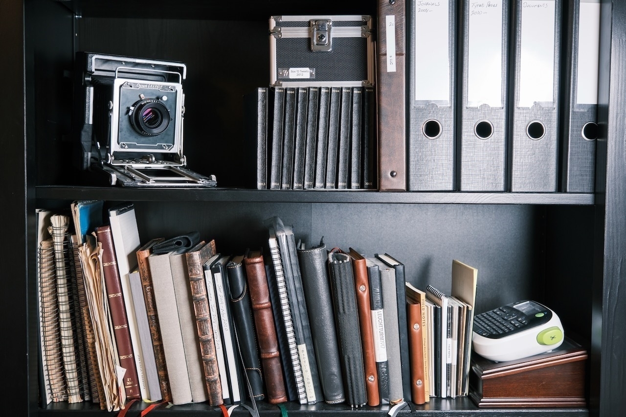 Camera and notebooks on bookshelves.